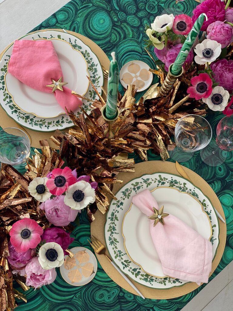 Tavola per Speciale Capodanno 2023 di Oltrelatavola.it con tovaglia a pattern malachite, centrotavola dorato con candele verde malachite e fiori rosa (anemoni e peonie)